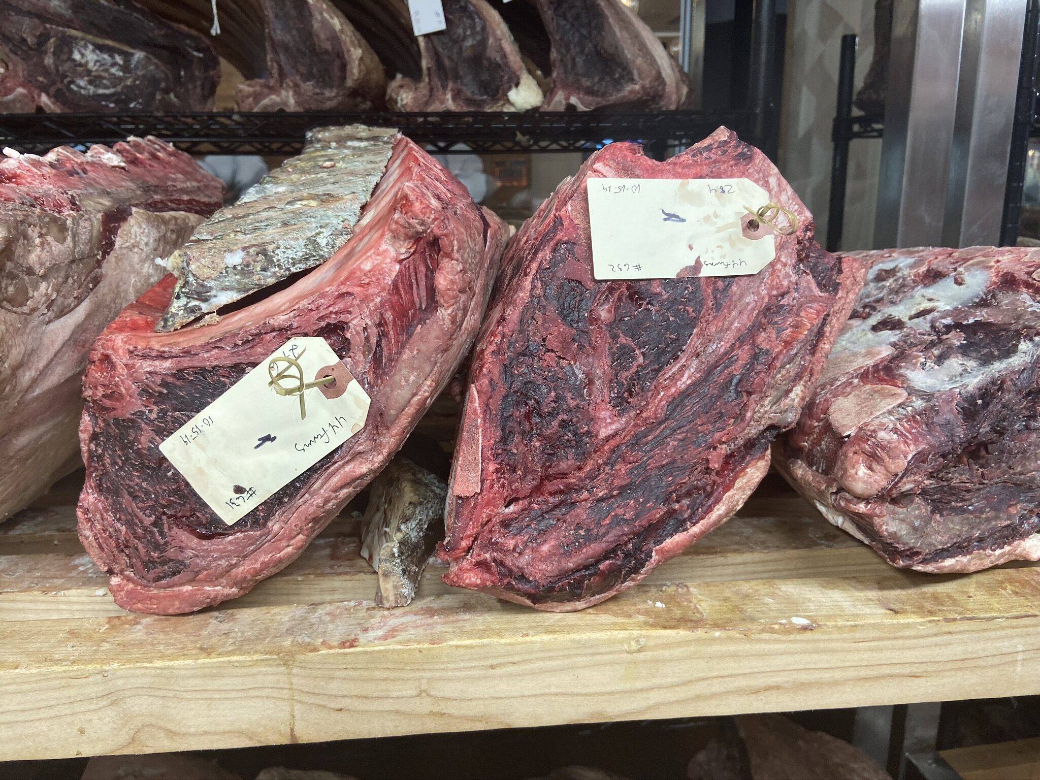 Hand-tagged, dry-aged rib primals on a shelf in the aging room