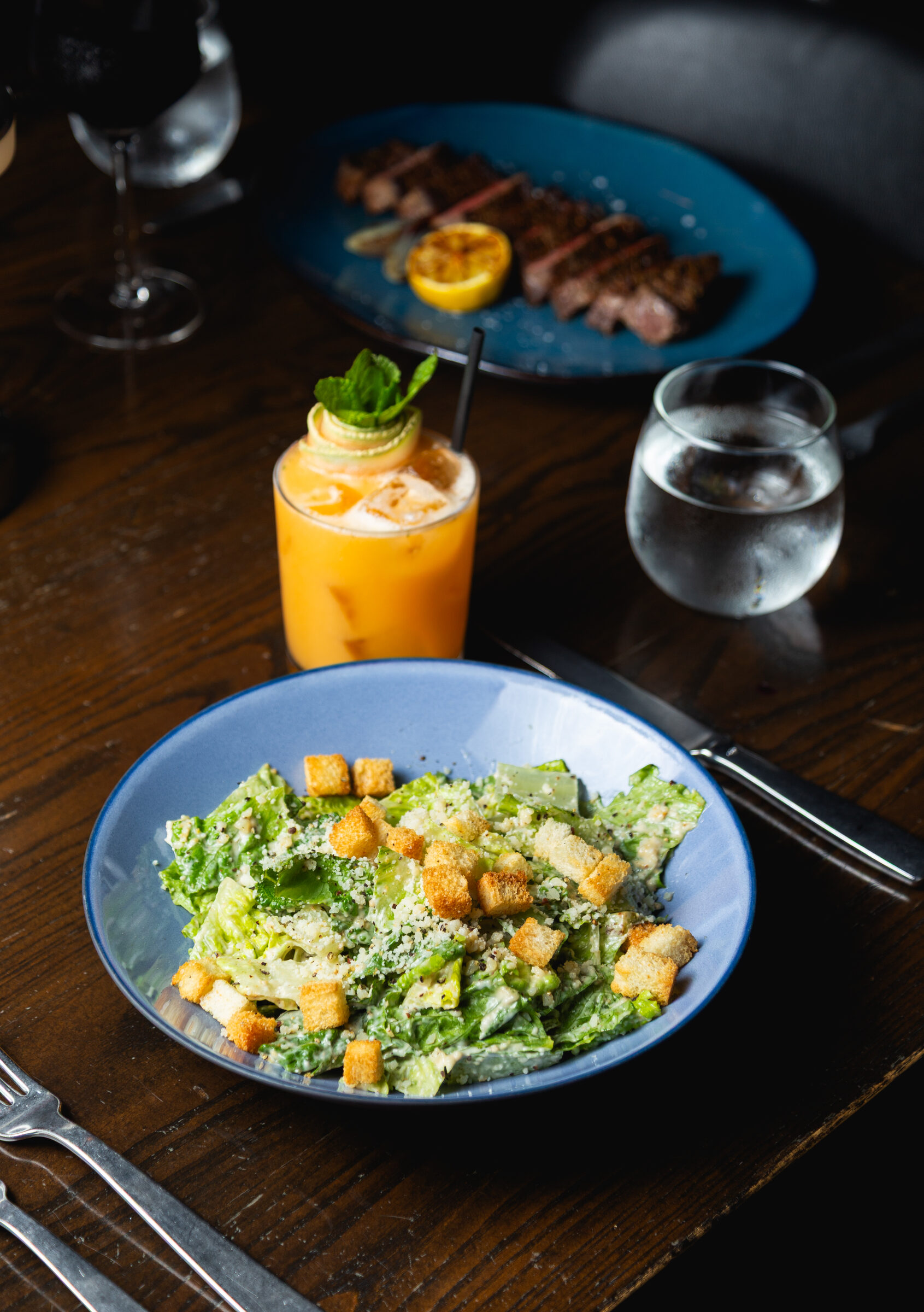A lunch table at Knife Steakhouse Plano — Classic Caesar, sliced steak, and a cocktail